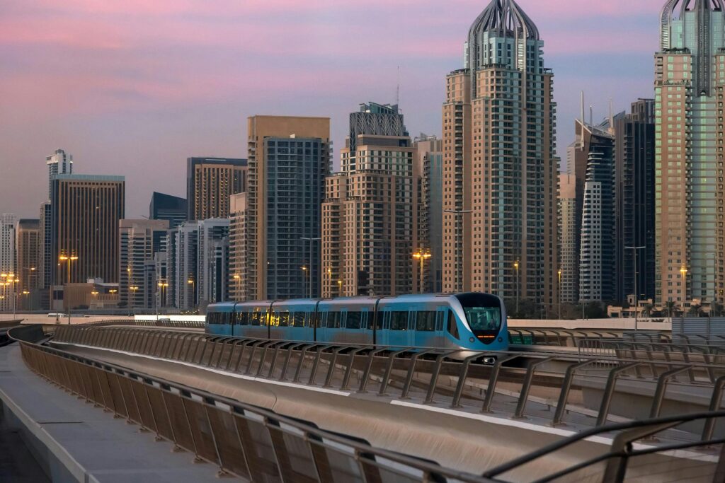 Futuristic Dubai Metro train traveling past modern skyline at sunset, capturing urban life and architecture.