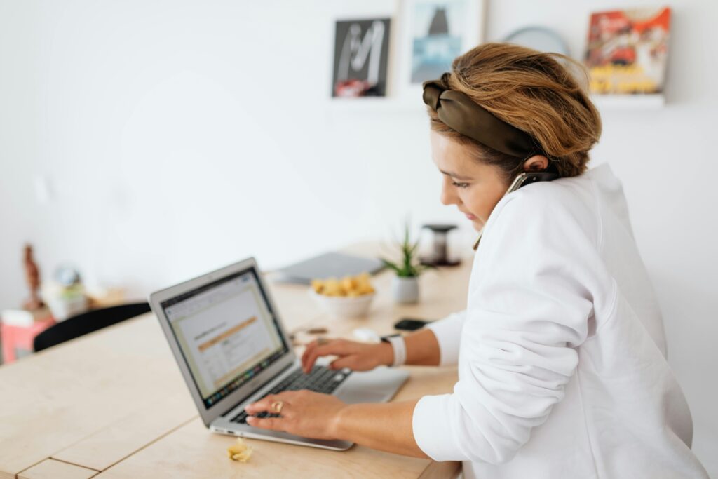 Focused woman multitasking, working on a laptop and phone in a modern home setting.