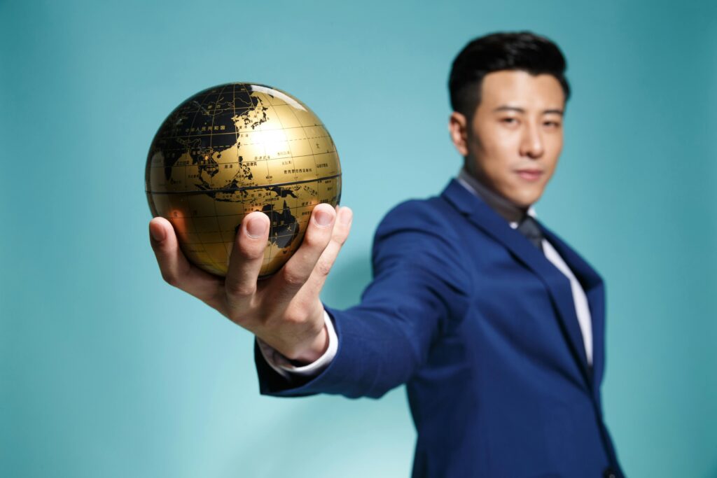 pexels photo 11264965 11264965 Asian businessman in blue suit confidently holding a golden globe against a blue background.