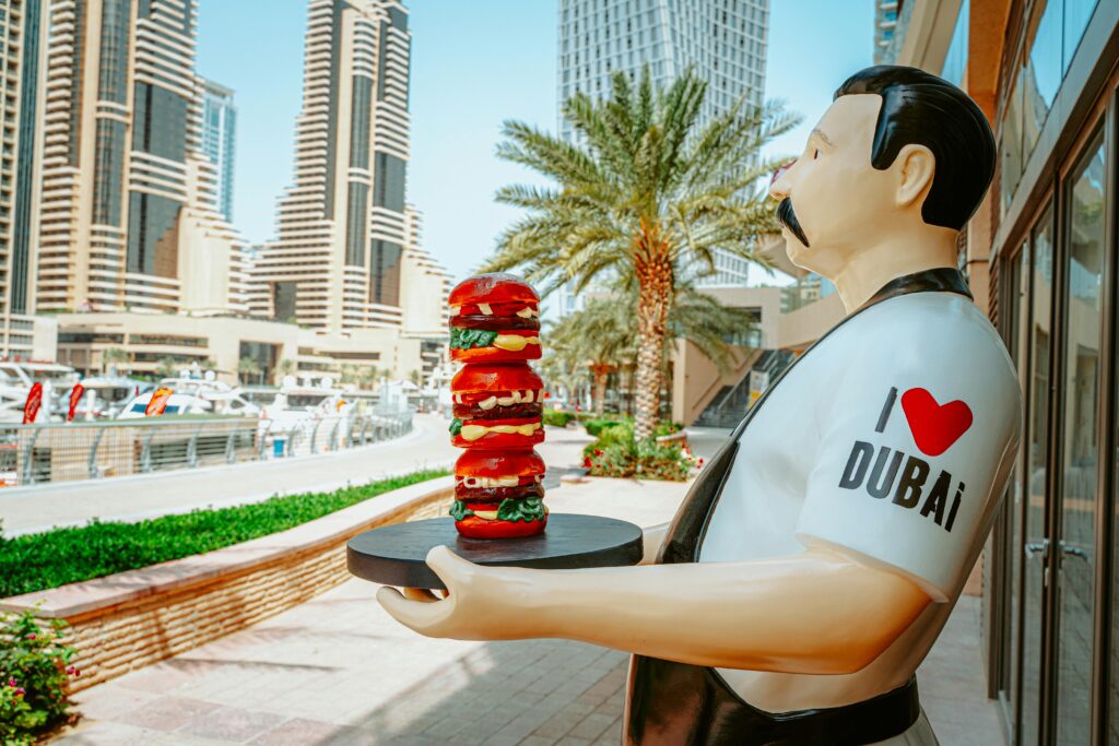 Statue of a man with a burger platter in vibrant Dubai urban area, with iconic architecture.
